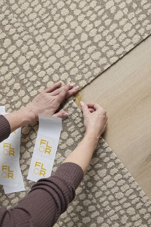 Hands of a person using a FLORdot to assemble a FLOR area rug from carpet tiles.